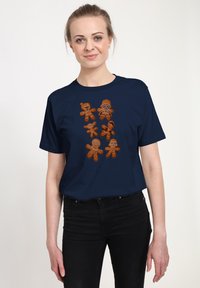 T-shirt bleu marine arborant six graphismes de bonhommes en pain d'épice stylisés en marron, chacun avec des designs et des expressions uniques. Tissu léger en coton.