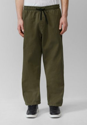 Olijfgroene, losse broek met een elastische tailleband en trekkoord. Glad materiaal met een rechte pijp, gestyled met zwarte sneakers.