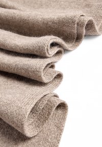 Šviesiai rudos mezgimo medžiaga, minkšta tekstūra, suvyniota keliuose sluoksniuose, demonstruojanti plonus siūlus ir subtilų raštą, priešingai baltam fonui.