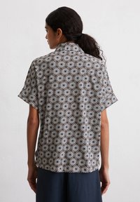 Short-sleeved shirt featuring a black and white geometric pattern with circular motifs on a light background, made of lightweight fabric.