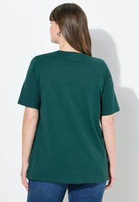 Tmavě zelené bavlněné tričko s krátkým rukávem, kulatým výstřihem a uvolněným střihem, zobrazené z pohledu zezadu na bílém pozadí.