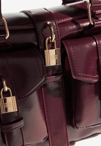 Bordo mākslīgās ādas somiņa ar zelta toņu aparatūru, kas aprīkota ar vairākiem kabatām, spīdīgu apdari un detalizētu izšuvumu.