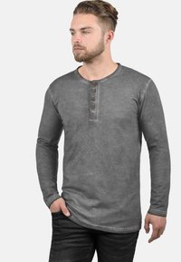 Graues Langarmshirt mit Rundhalsausschnitt und einer Knopfleiste mit fünf Knöpfen. Weicher, verblasster Stoff mit glatter Textur. Mit geraden Ärmeln gestaltet.