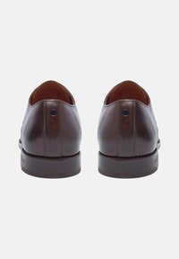 Braune Lederschuhe mit glatter Oberfläche, abgerundetem Absatz und einem kleinen Logoakzent nahe der Ferse. Flache Sohlen und genähte Konstruktion.