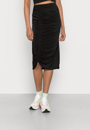 Saia midi preta com franzido, tendo uma costura lateral gather e uma fenda. Combinada com ténis brancos e em tons pastel, apresentando um design texturizado e toques de cor vibrantes.
