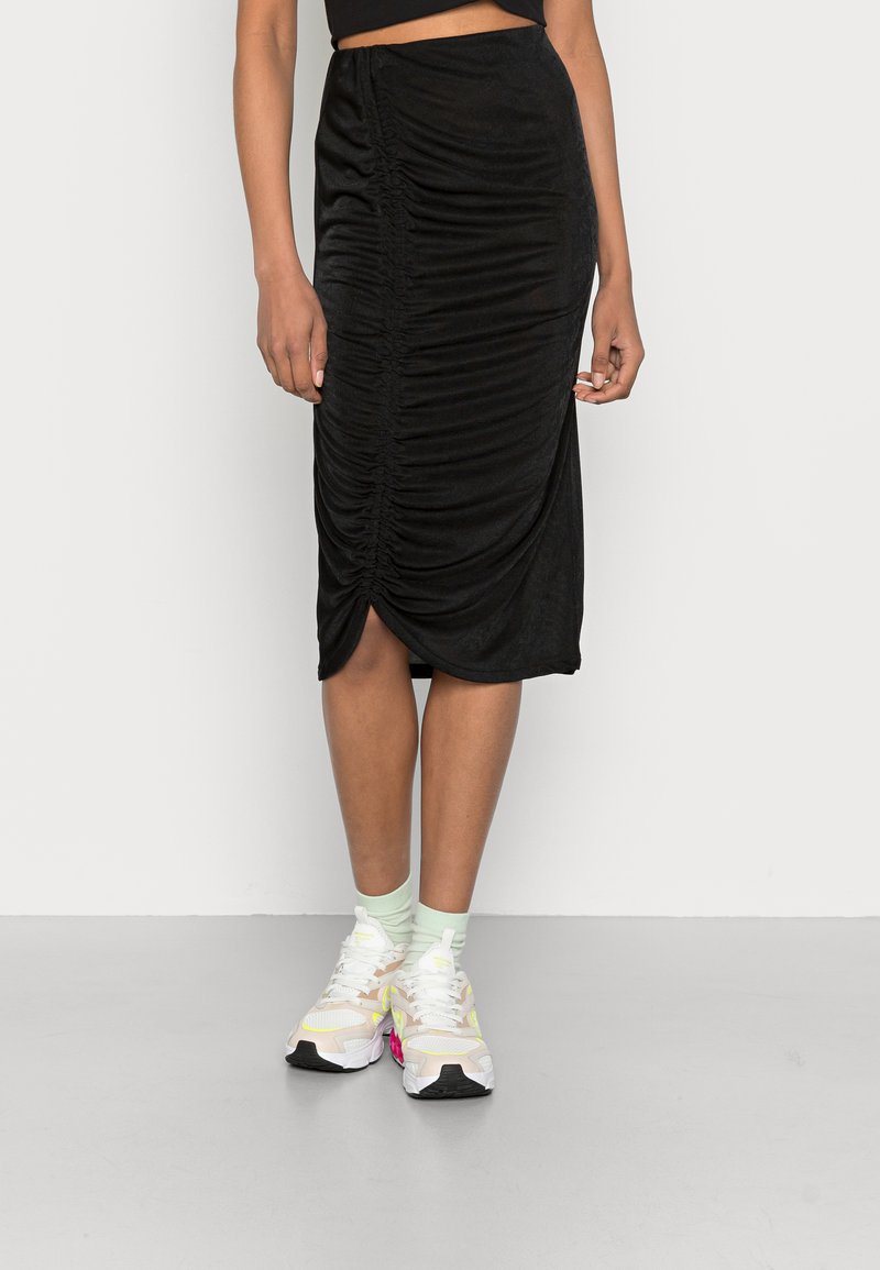 Saia midi preta com franzido, tendo uma costura lateral gather e uma fenda. Combinada com ténis brancos e em tons pastel, apresentando um design texturizado e toques de cor vibrantes.