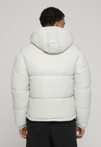 Pūka jaka gaisā pelēkā krāsā ar kapuci. Iespējas ietver iešūtas sadaļas, elastīgas aproces un gludu tekstūru ar modernu griezumu.