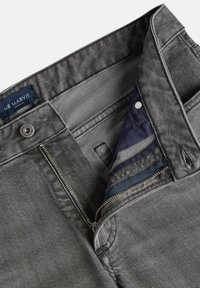 Grijze denim broek met een zichtbare rits, knoopsluiting en etiket van stof. De binnenvoering heeft strepen in blauw en grijs. Zachte textuur.