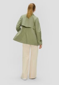 Olive green lightweight jacket with a layered back design, long sleeves, and button accents, paired with cream wide-leg trousers.