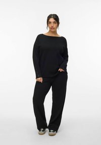 Czarny, dziany, oversize sweter z guzikami na rękawach oraz dopasowanymi czarnymi, szerokimi spodniami. Miękka tekstura, luźny krój i minimalistyczny design.