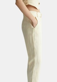 Pantaloni su misura di un giallo chiaro, realizzati in un tessuto liscio e testurizzato. Presentano una silhouette aderente e tasche laterali, completati da una cintura coordinata.
