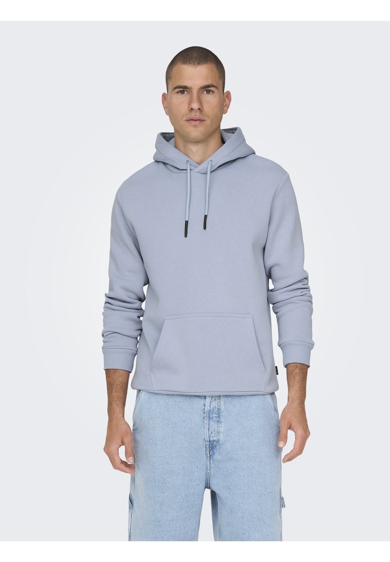 Sudadera ligera gris claro hecha de una tela suave, que presenta un bolsillo frontal, capucha con cordón y puños de canalé. Combinada con pantalones cortos de mezclilla azul claro.