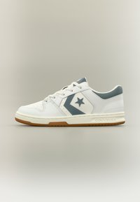 Άσπρο αθλητικό παπούτσι Converse χαμηλού προφίλ με γκρι αστέρι και λογότυπο σχήματος βέλους, μπροστινό κορδόνι, μαλακό πέλμα και εξωτερική σόλα από καουτσούκ καραμέλας.