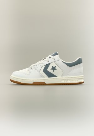 Hvit lavt snaut Converse-sneaker med grå stjerne- og chevron-logo, snøring foran, polstret såle og gummiyttersåle.