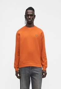 Orange sweatshirt with a round neck and long sleeves. Features a small yellow butterfly logo on the chest. Paired with dark denim jeans.