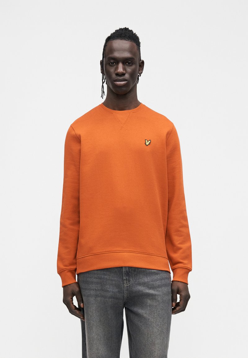 Orange sweatshirt with a round neck and long sleeves. Features a small yellow butterfly logo on the chest. Paired with dark denim jeans.
