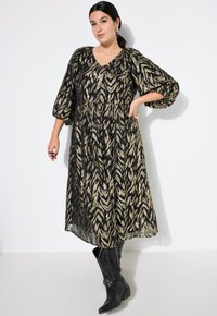 Mekko, jossa on musta ja kultainen kuvio, lyhyet puffihihat, V-kaula-aukko, kerätty vyötärö ja lentävä hame, yhdistettynä polven yli ulottuviin mustiin saappaisiin.