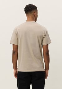 Beige bomulls-T-skjorte med korte ermer, rund hals og en ledig passform. Glatt tekstur uten synlige mønstre eller detaljer.