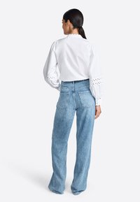 Blusa di cotone bianca con colletto a volant e maniche in broderie anglaise, abbinata a jeans flare in denim blu a vita alta.