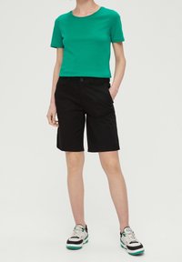 Grön bomullströja med rund hals i kombination med svarta knälånga shorts. Sneakers med gröna detaljer fulländar outfiten.