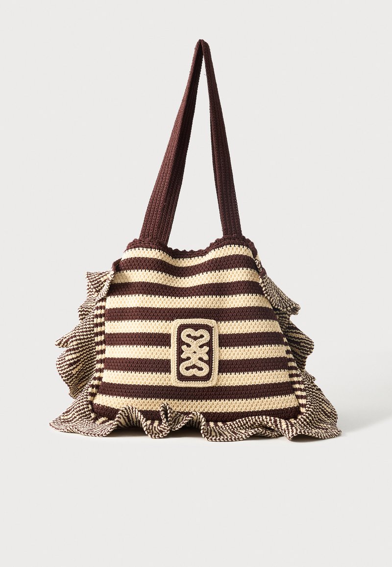 Καφέ και μπεζ ριγέ τσάντα tote από πλεξούδα με μακριές λαβές και βολάν στο κάτω άκρο, με κεντρικό διακοσμητικό πλεκτό έμβλημα.