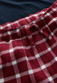 Röd och vit rutigt flanelltyg med elastisk midja och rosett. Bakgrunden har en mörkblå enfärgad färg.