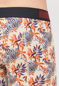 Badehosen mit einem Blumendesign in Orange, Rosa und Blau auf einem beigen Hintergrund; elastischer Bund in Marineblau und Maroon.