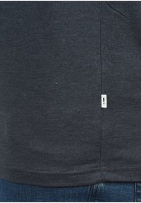Mørkegrå bomulds t-shirt med en subtil tekstur, der har et lille hvidt mærke med et udråbstegn på sømsiden og en lige kant.