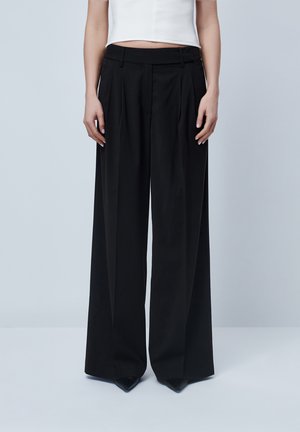 Black wide-leg trousers with a high waistband, featuring front pleats and a smooth texture. Paired with pointed black shoes.
