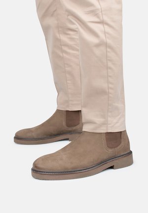 Botas Chelsea de ante marrón con paneles laterales elásticos y suelas de goma, con punta redondeada y costuras en contraste.