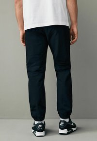 Sorte sportlige joggere med elastiske manchetter, parret med sorte og hvide Nike sneakers. Materialet ser glat ud, med en afslappet pasform.