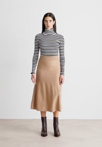 Pruhovaný rolák v čiernej a bielej farbe, kombinovaný s priliehavou béžovou pletenou midi sukňou. Hnedé kotníkové čižmy dotvárajú celý outfit.