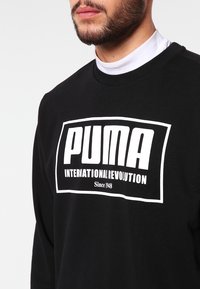 Felpa nera con un grande logo bianco "PUMA" e la scritta "INTERNATIONAL REVOLUTION". Realizzata in cotone con design a collo rotondo.