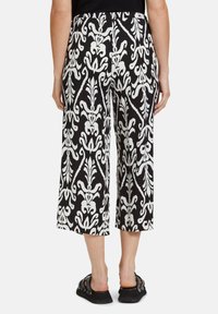 Schwarz-weiße gemusterte weit geschnittene Hosen mit einem dekorativen Blumenmuster, aus einem leichten Stoff gefertigt, mit einem hohen Bund.