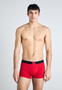 Rote Boxershorts aus weichem Stoff, mit einem schwarzen elastischen Bund mit Logo-Detail. Figurbetontes Design, glatte Textur, in Knielänge.