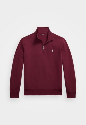 Burgundijas krāsas abrāžu ar rāvējslēdzēju, ar augstu apkakli, garām piedurknēm, ribotām aprocēm un baltu izšūtu lojā uz krūšu daļas. Gluda auduma tekstūra.