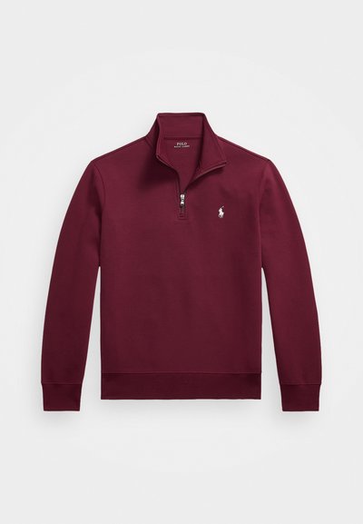 Burgundiborgozi cipzáros pulóver magas nyakkal, hosszú ujjakkal, bordás mandzsettákkal és fehér hímzett logóval a mellkason. Simább anyag szerkezete.