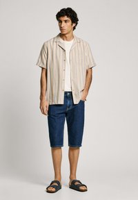 Korte mouwen gestreepte shirt in lichtbeige met blauwe en oranje strepen, gecombineerd met donkerblauwe denim shorts en zwarte sandalen.