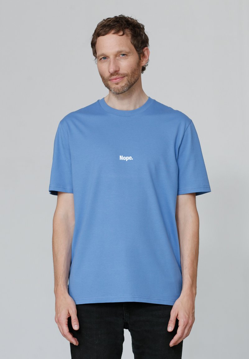 T-shirt en coton bleu à manches courtes et col rond. Présente l'inscription "Non." en texte blanc sur le devant. Porté avec un jean foncé.