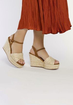 Sandalias de cuña con plataforma de material de paja trenzada y correas de cuero marrón. Diseño cerrado en la punta con correa ajustable en el tobillo.