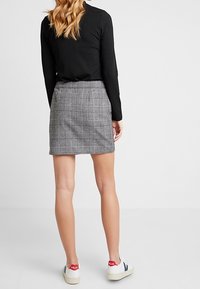 Svart ribbat långärmad topp i kombination med en grå rutmönstrad kjol. Vita sneakers med röda och marinblå accenter. Tydlig och strukturerad silhuett.