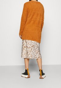Pomarańczowy puszysty sweter, biała spódnica midi w brązowy nadruk w cętki oraz czarne wysokie trampki z białymi podeszwami i pomarańczowymi akcentami.