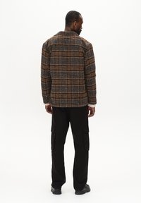 Ruitpatroon in bruin en beige jasje met textuur, voorzien van een kraag en gebuttonde manchetten, gecombineerd met zwarte cargobroek en stevige zwarte laarzen.
