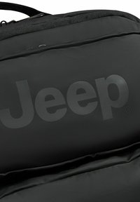 Zaino nero con una superficie texturizzata, caratterizzato da un grande logo riflettente "Jeep", compartimento con cerniera e tessuto resistente.