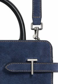 Borsa in denim blu con manici in pelle nera. Presenta accessori in metallo argentato e un accento decorativo a forma di T. I dettagli delle cuciture visibili mettono in risalto il design.
