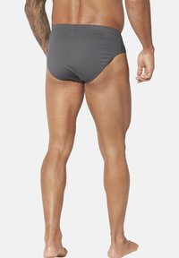 Graue Herren-Badebriefe mit einem hoch ausgeschnittenen Bein-Design, weichem Stofftextil und minimalen Nähdetails, von hinten betrachtet.