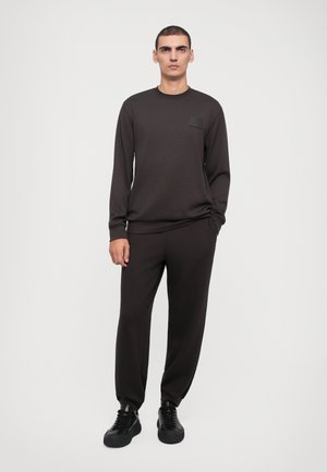 Dark brown sweatshirt with a crew neck and long sleeves, paired with matching tapered pants and black sneakers, set against a plain background.