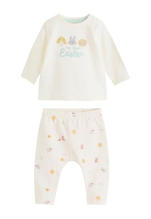 Crèmekleurige babyoutfit met een longsleeve top met paaskuiken, konijn en ei ontwerpen, en bijpassende broek met kuikens en zonnetjes patroon.