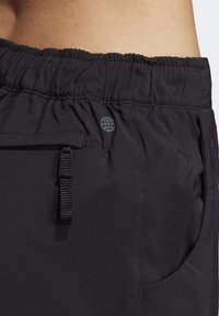 Černé kalhoty s elastickým pasem, se zipovou kapsou a malým logem globu blízko pasu na kyčli a dolní části zad osoby.