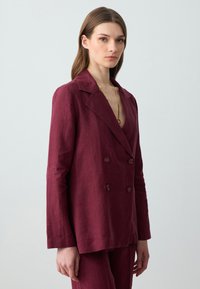 Dwurzędowa marynarka w ciemnym burgundzie z lnu, z klapami, długimi rękawami i guzikami, zestawiona z dopasowanymi spodniami.